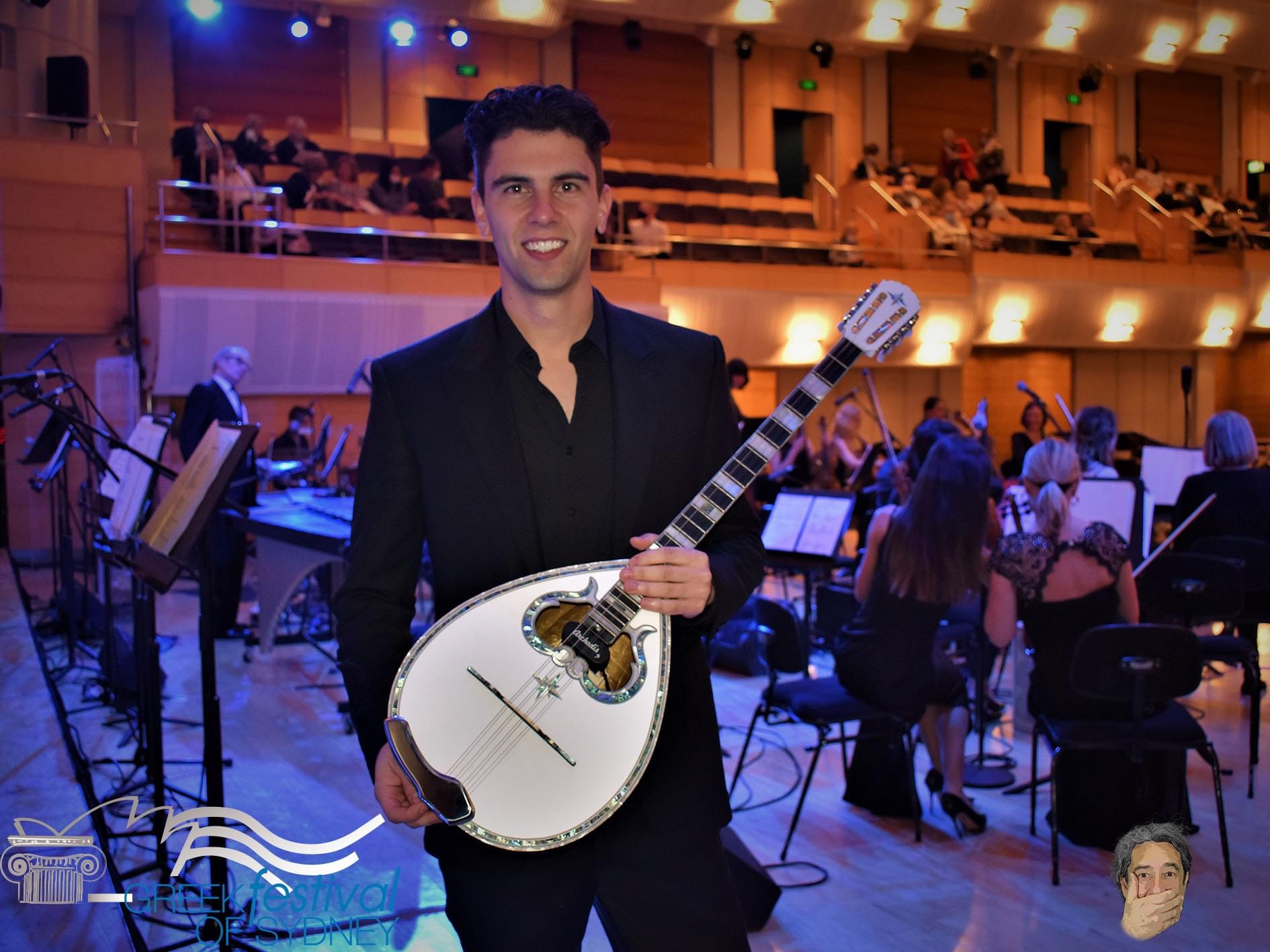 Perry Tsepetzis smiling and holding his bouzouki in a concert hall